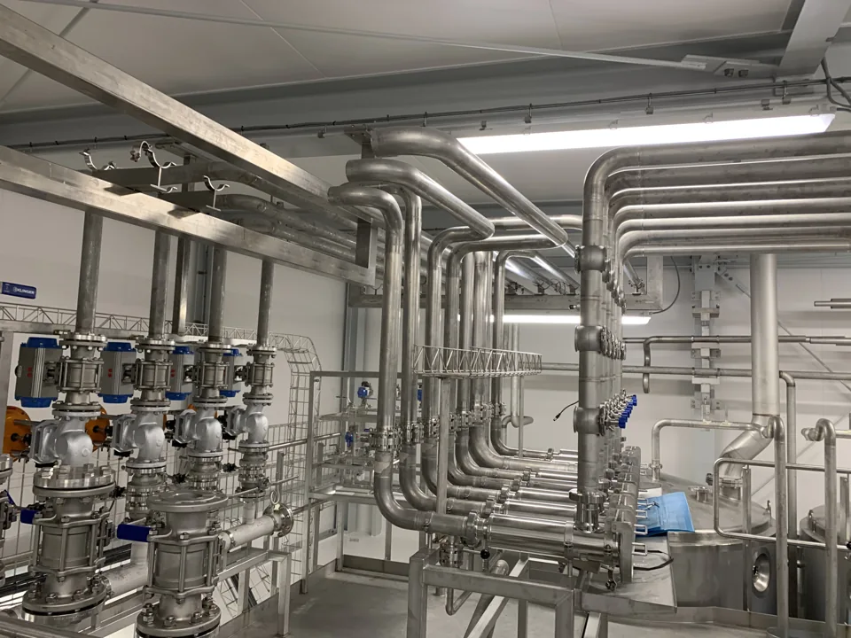 RVS-leidingwerk met bochten en afsluiterunits in een witte productieruimte