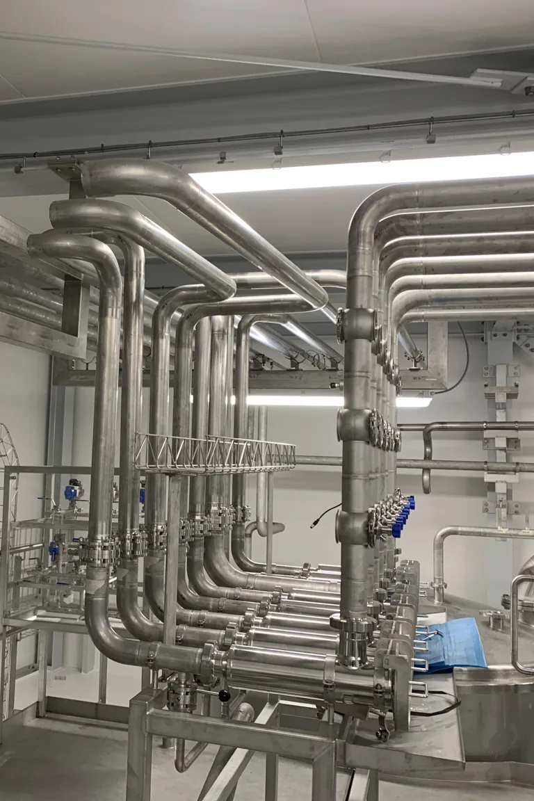 RVS-procesleidingwerk met aangedreven afsluiters en leidingbogen in een witte productieruimte