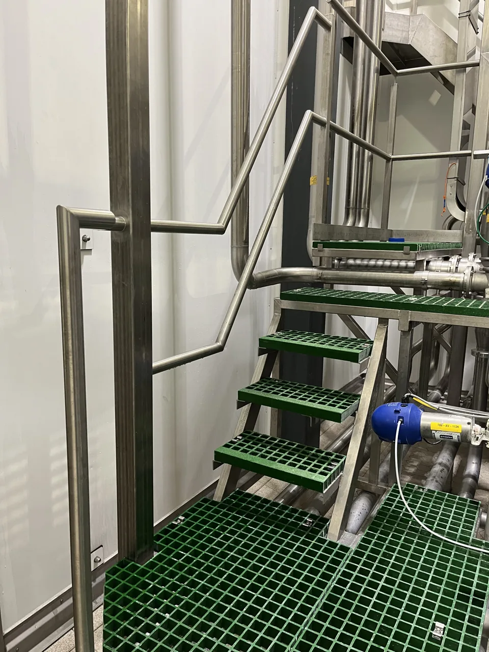 Groen roosterbordes met trap en RVS-leidingwerk op een skid